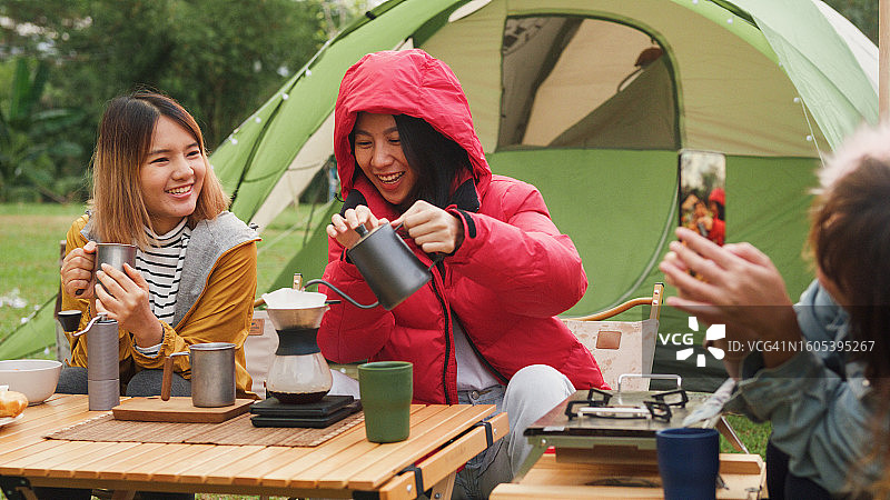 年轻的亚洲女性在度假时用智能手机给朋友拍照，早上在露营车里用水浇在咖啡粉上。生活方式旅行。图片素材