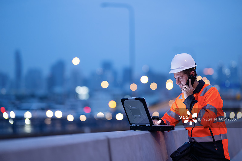 通过施工管理软件实现更好的沟通与协作，获得项目实时洞察：项目经理在悬索桥施工现场使用笔记本电脑，并通过电话与团队讨论项目任务。图片素材