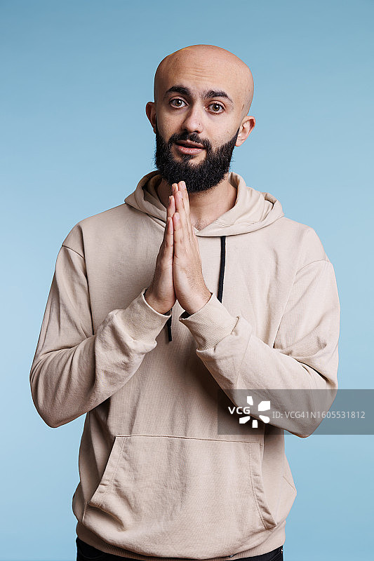 在蓝色背景前祈祷的年轻男人肖像图片素材