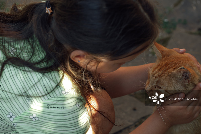 快乐的小女孩在户外抚摸橙色猫咪图片素材