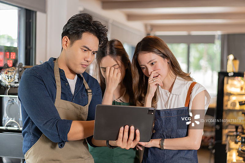 咖啡店里咖啡师创业团队会议：年轻的亚洲男女咖啡馆员工认真地用平板电脑进行讨论图片素材