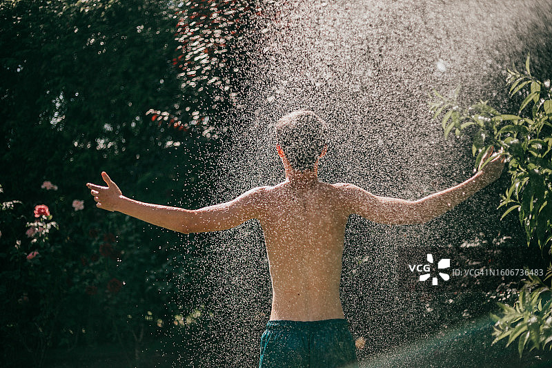 青少年在炎热的夏天被软管喷洒的背面图像图片素材