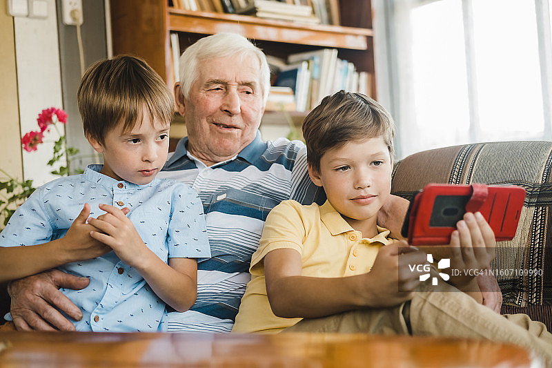 爷爷和孙子们坐在沙发上，用智能手机观看有趣的视频图片素材