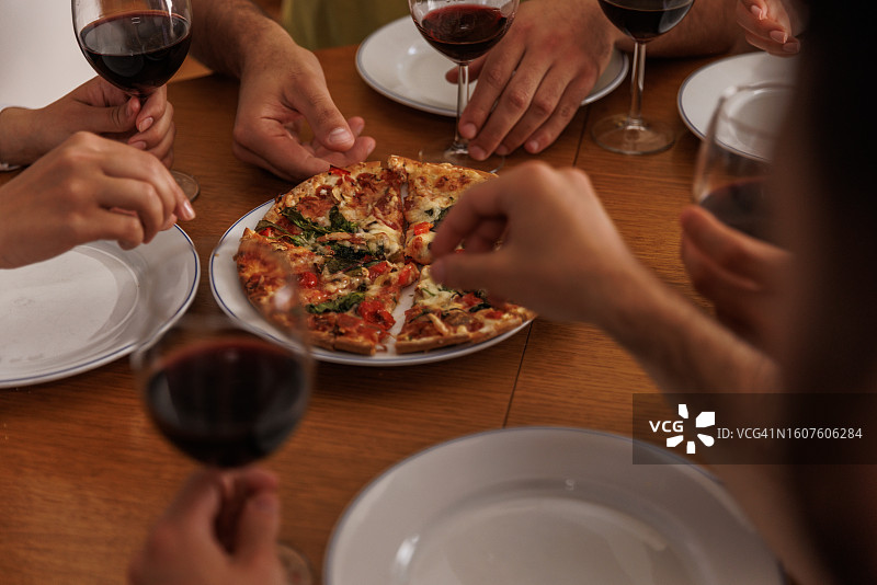 朋友们伸手去拿桌子上美味的披萨图片素材
