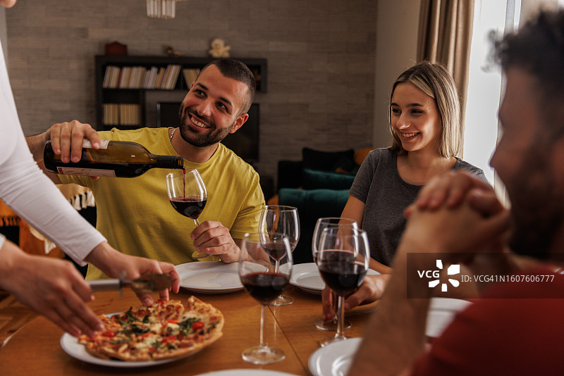男人倒酒与朋友一起享用披萨图片素材