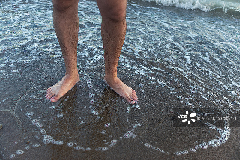 男人双脚站在海水中的沙滩上图片素材