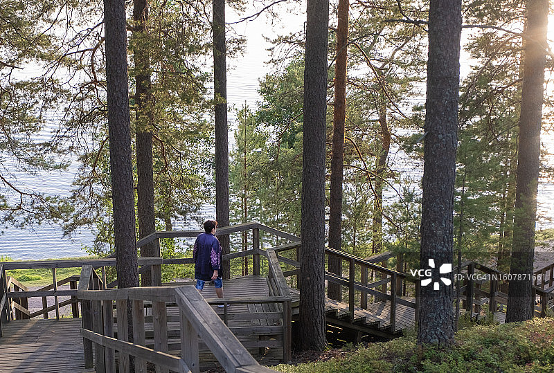 一位77岁的老年妇女在傍晚散步，在湖边的自然环境中。一位妇女在湖边走下木梯。图片素材