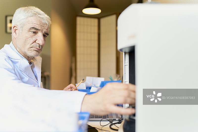 男子身穿实验服坐在办公桌前从扫描仪中取东西的侧视图图片素材