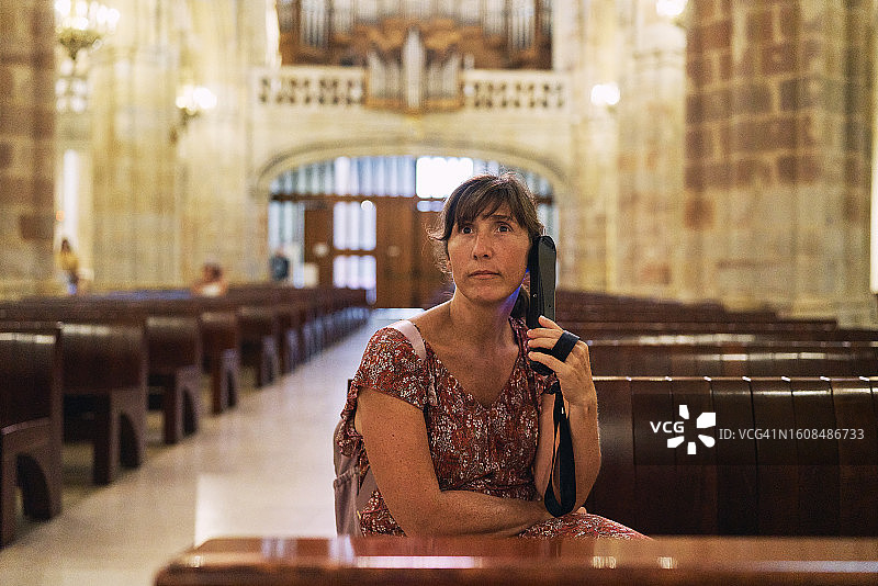 坐在大教堂里，拿着手机对着镜头微笑的女人肖像图片素材