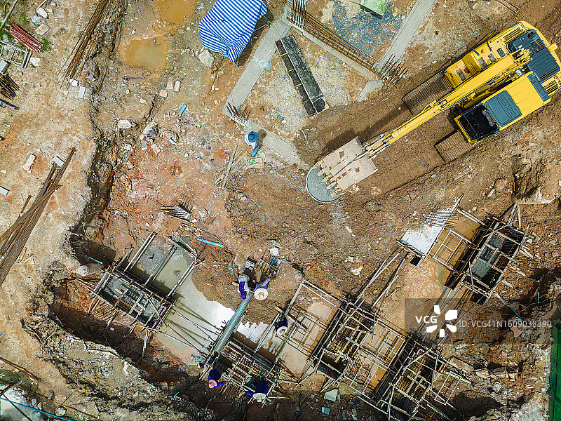施工现场：挖掘机辅助工人吊装钢材，构建地基图片素材