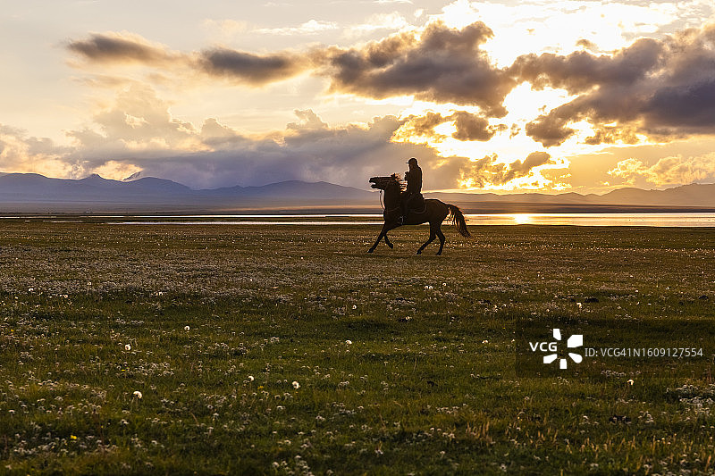 在吉尔吉斯斯坦宋科尔湖岸边日落时分的骑马者图片素材