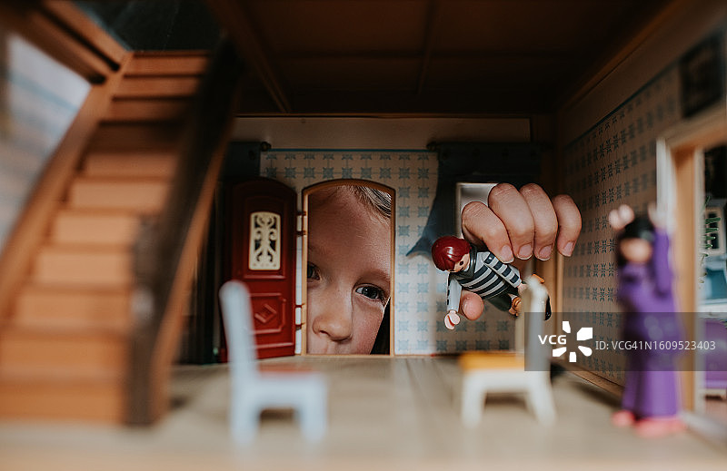 小女孩透过玩偶屋的门看着里面的家具和玩偶图片素材