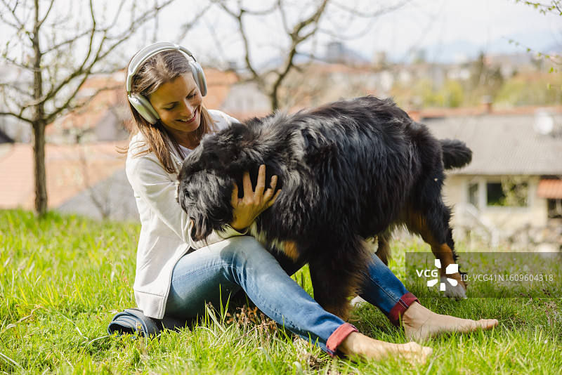 在阳光明媚的日子里，快乐的女人在公园里和狗狗一起玩耍，一边听音乐图片素材