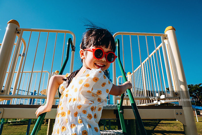 快乐的亚洲小女孩在阳光明媚的户外游乐场玩耍。 笑着看着镜头。 户外乐趣。 无忧无虑和自由的概念图片素材