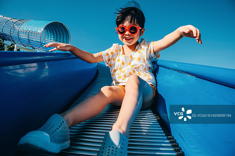 快乐的亚洲小女孩在阳光明媚的户外游乐场玩滑梯图片素材
