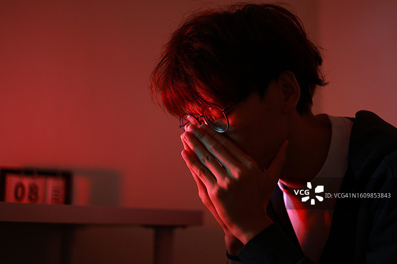 一位年轻的亚洲成年男子，深夜坐在床上，闭着眼睛，陷入沉思，思考如何解决生活中的问题，看起来明显沮丧图片素材