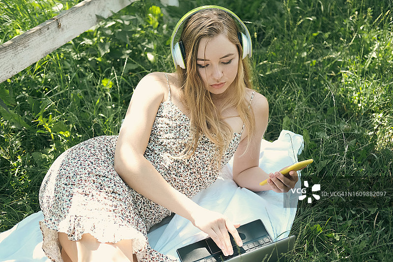 年轻女人在绿色的草地上使用超极本和智能手机图片素材