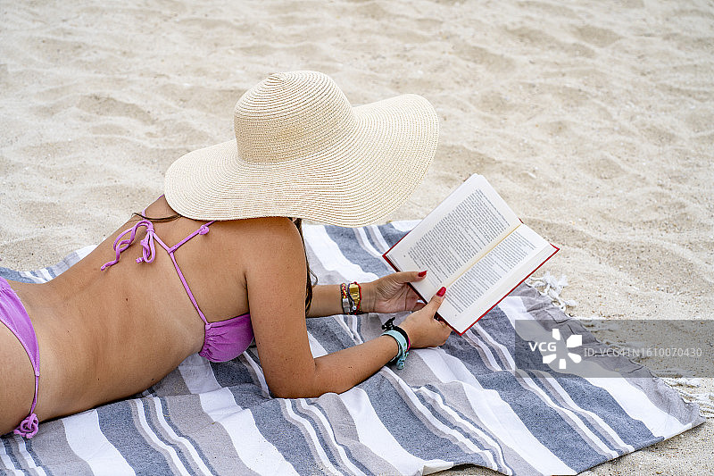 在海滩上读书的年轻黑发女子肖像图片素材