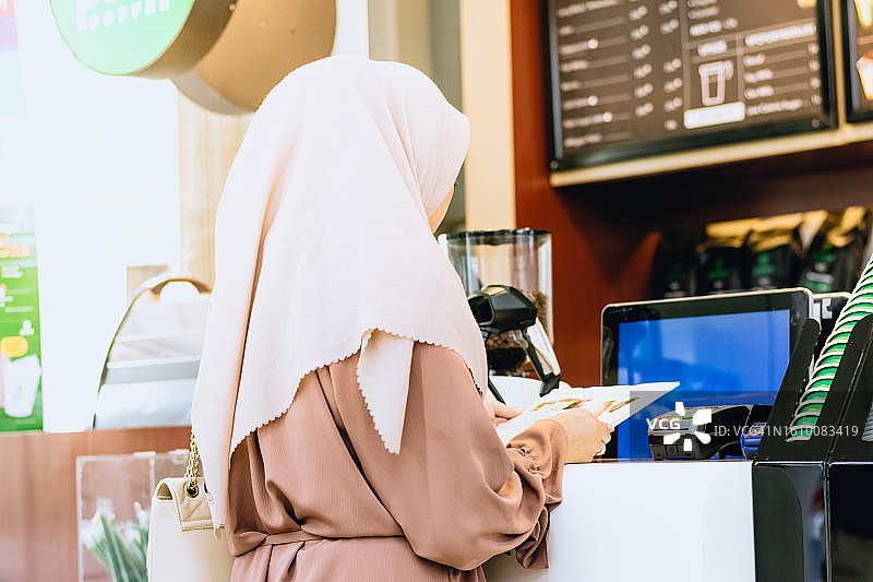 年轻的亚洲穆斯林女性在咖啡店付款购买咖啡的背影图片素材