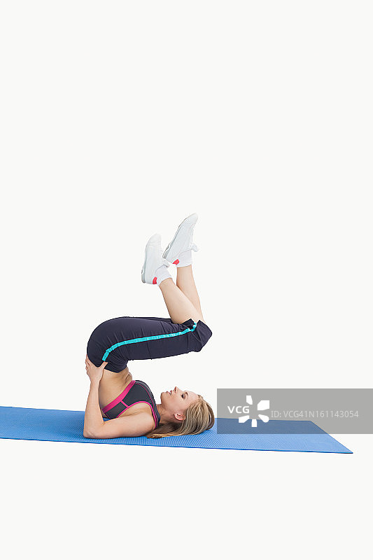 年轻女子在瑜伽垫上做肩倒立侧视图图片素材