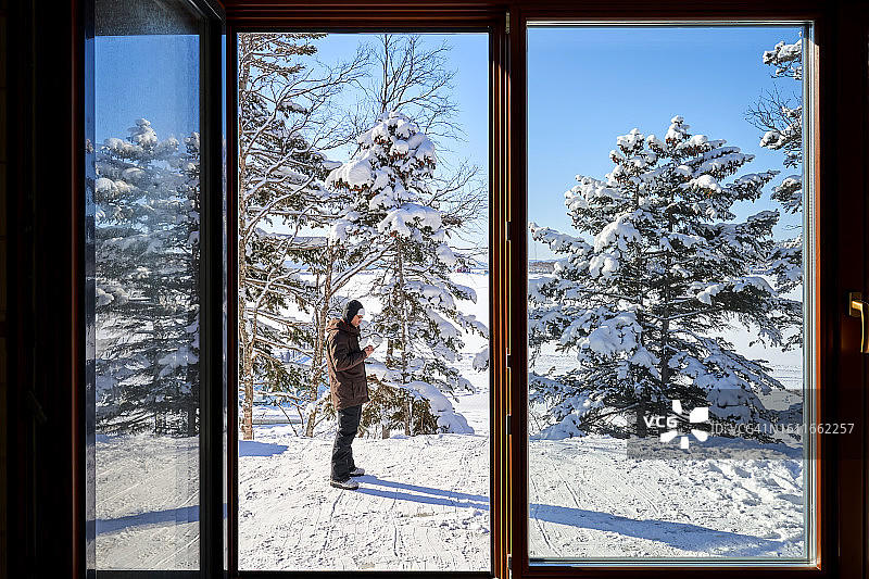 站在窗外，以雪景为背景，看着手机的男人图片素材