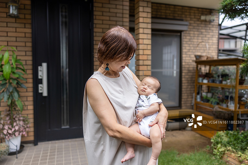 祖母抱着孙子站在房子入口前图片素材