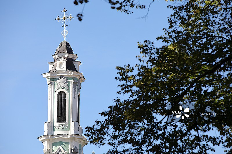 教堂尖顶塔，十字架与蓝天，前景有树图片素材
