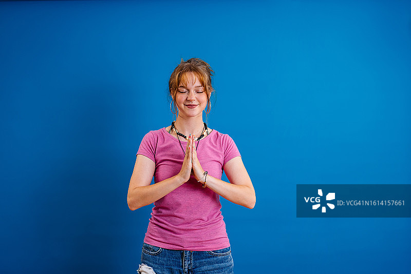 在蓝色背景下手持祈祷姿势的年轻女人图片素材