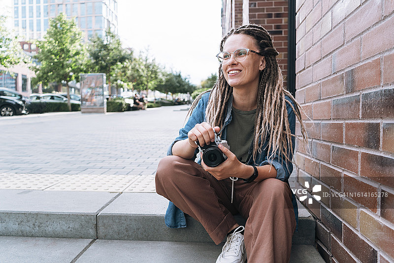 在城市街道台阶上拿着相机的微笑脏辫女摄影师肖像图片素材