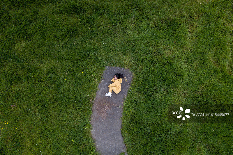 黄色运动服女孩躺在草地混凝土路沿上航拍视角图片素材