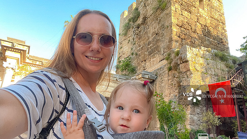 在土耳其安塔利亚古城旅行并探索著名的哈德良拱门时，抱着女婴自拍的女人图片素材