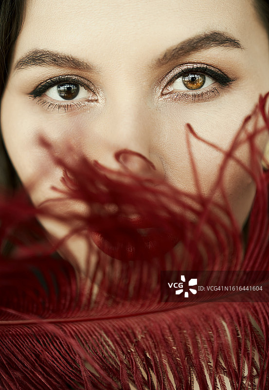 虹膜异色症：拥有不同眼睛的美丽女人特写，红唇和红色羽毛，温柔和女性问题概念，带复制空间。图片素材