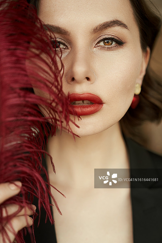 虹膜异色症：拥有不同眼睛的美丽女人特写，红唇和红色羽毛，温柔和女性问题概念，带复制空间。图片素材