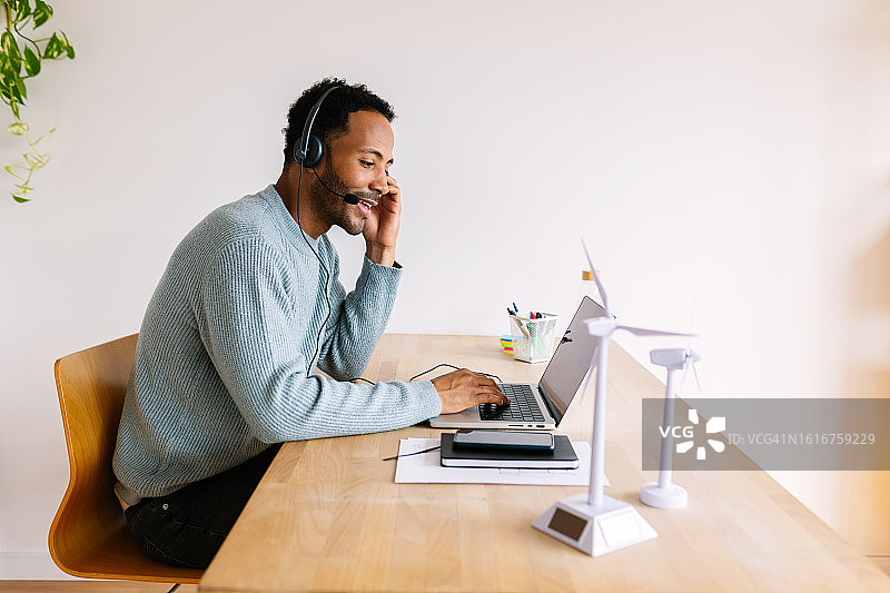 微笑的商务男士戴着耳机在办公室用笔记本电脑工作，提供客户服务和技术支持图片素材