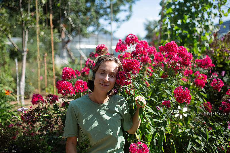 戴着耳机闻粉色鲜花的女人图片素材