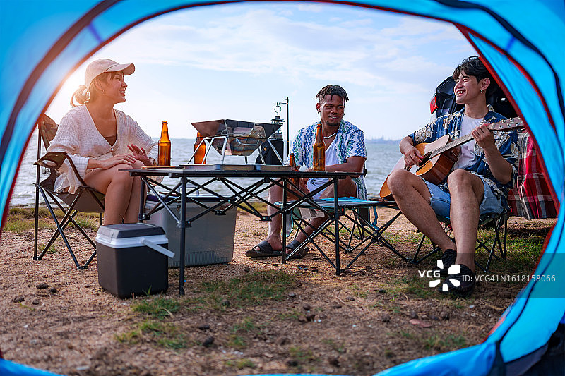 一群青少年在海滩上玩耍和弹吉他，露营，旅行概念图片素材