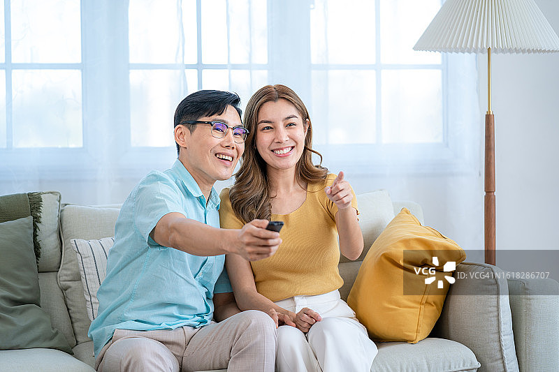 男人和妻子在家中沙发上放松，手持遥控器图片素材