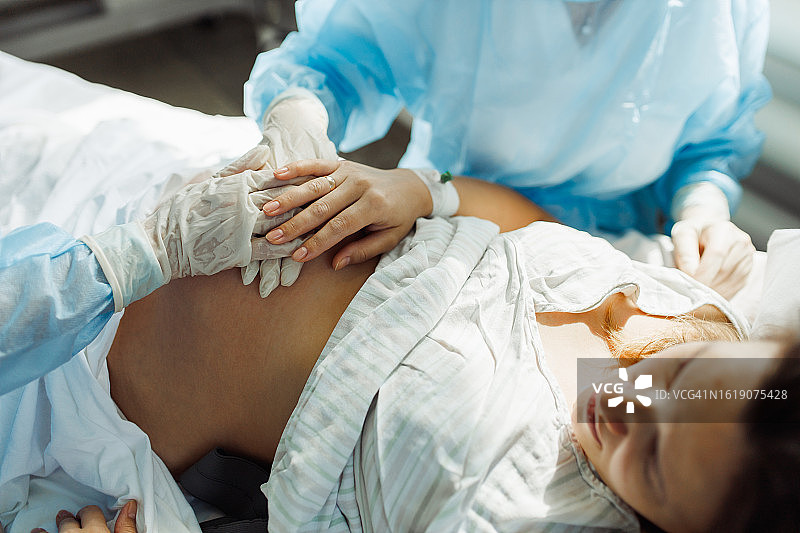 孕妇在床上分娩，两位经验丰富的女医生在一旁看护（高角度）图片素材