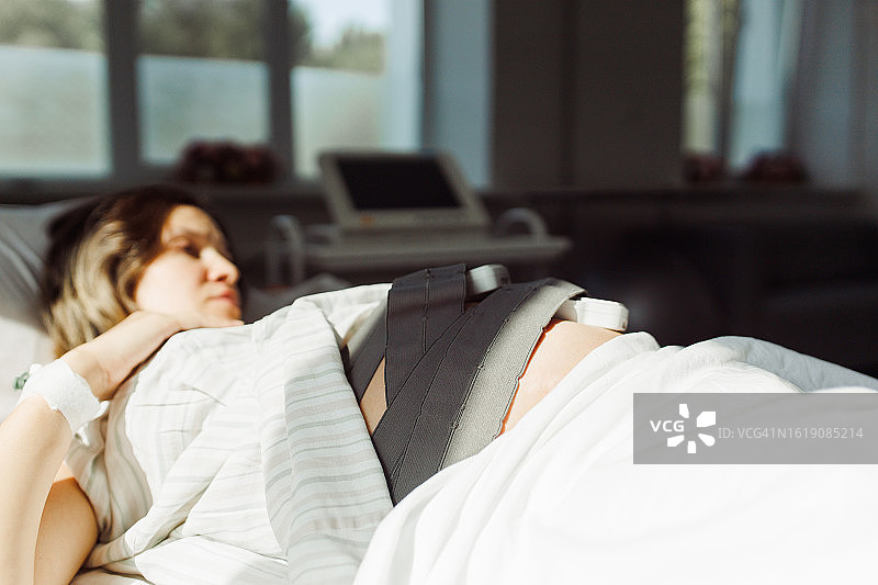 宁静的孕妇躺在床上，腹部放着心跳监测设备图片素材