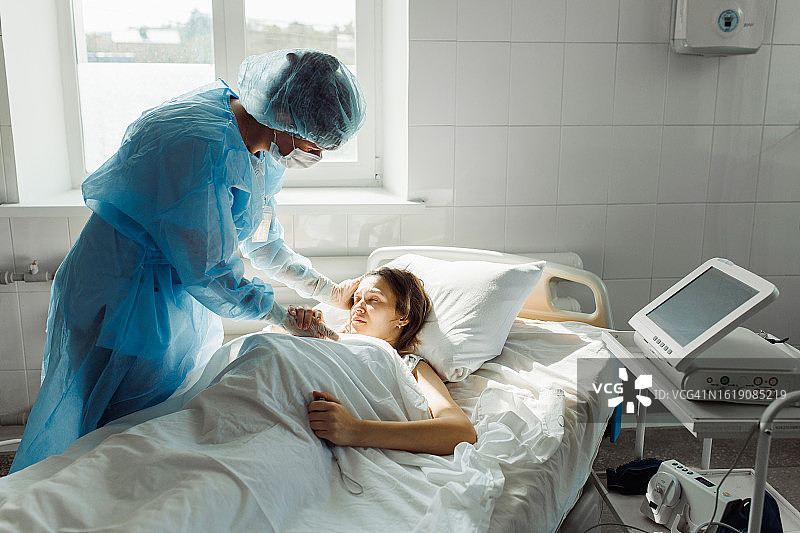富有同情心的中年女护士俯身在病床上，握着手向准妈妈表达支持图片素材