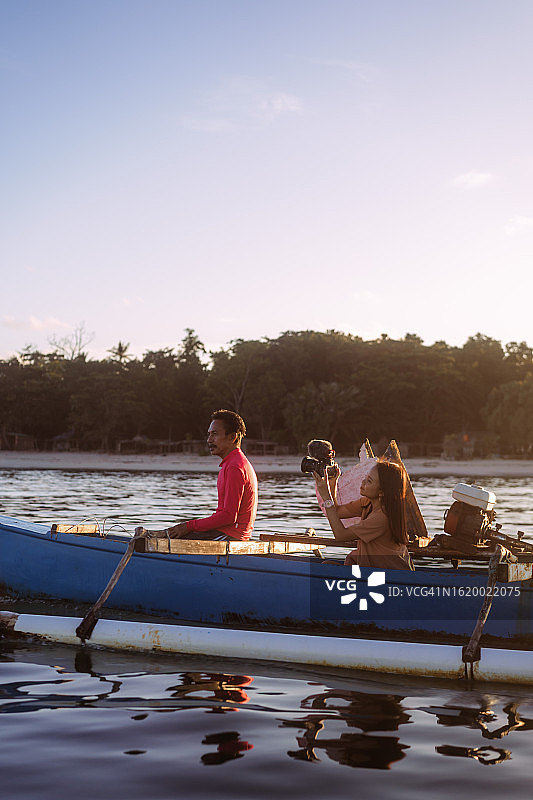 亚洲女游客拍摄渔民乘木船捕鱼图片素材