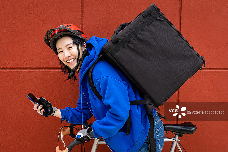 骑自行车手持手机微笑的送货女人图片素材