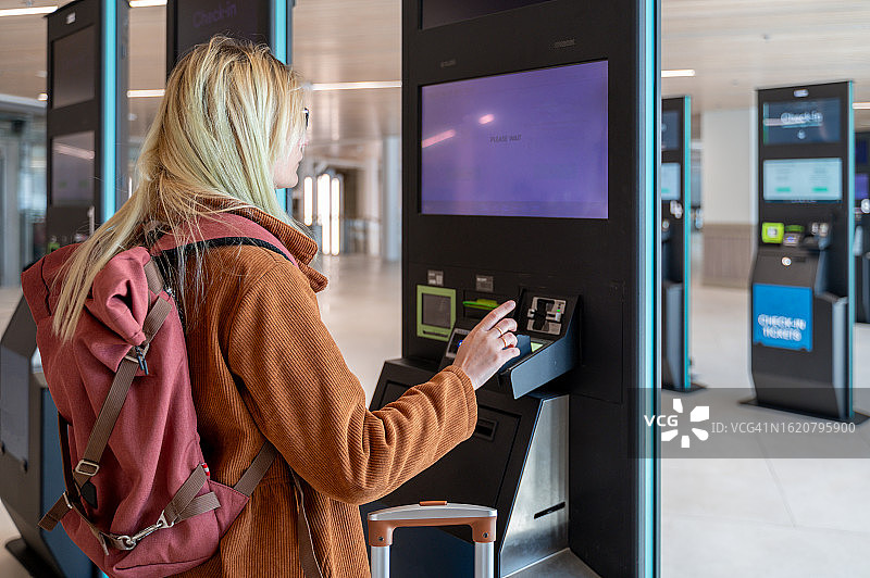 身穿棕色斗篷、拖着行李箱在客运站办理登机的女人图片素材