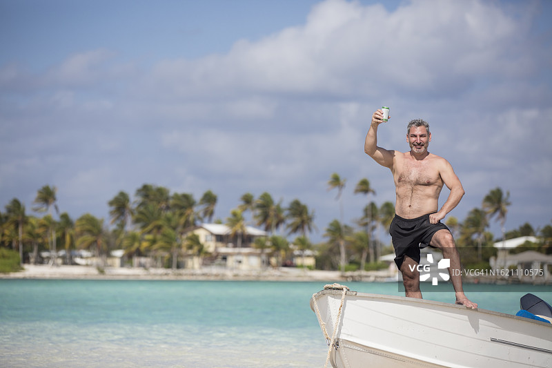 自信的男人站在白色小船上，背景是加勒比海沿岸风光图片素材