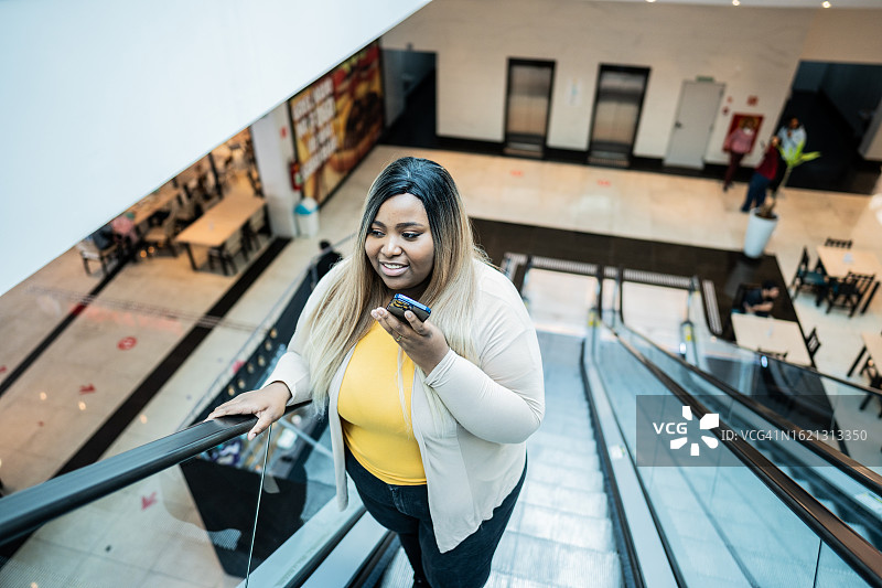 年轻女人在购物中心乘坐自动扶梯时用手机发送语音消息图片素材
