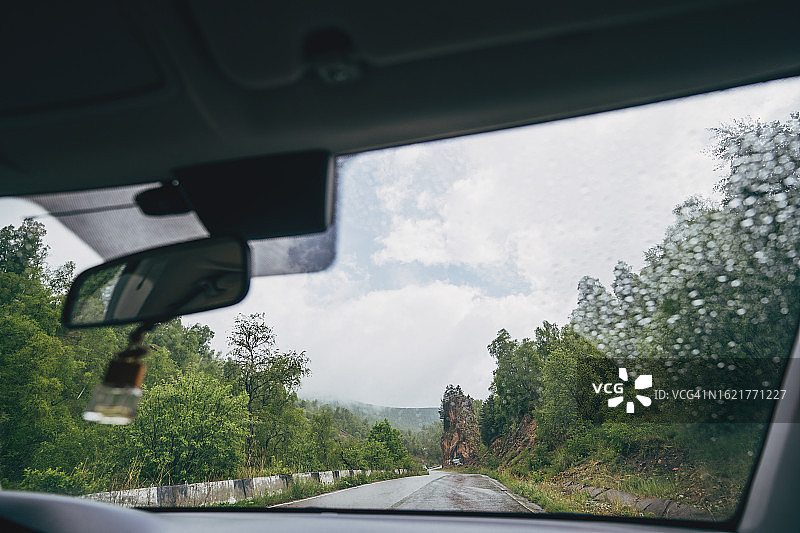 在空旷的道路上行驶，透过汽车挡风玻璃可以看到远处的群山和多云的天空图片素材