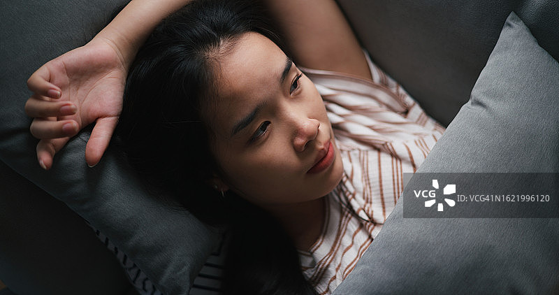 躺在沙发上思考的年轻亚裔女性图片素材