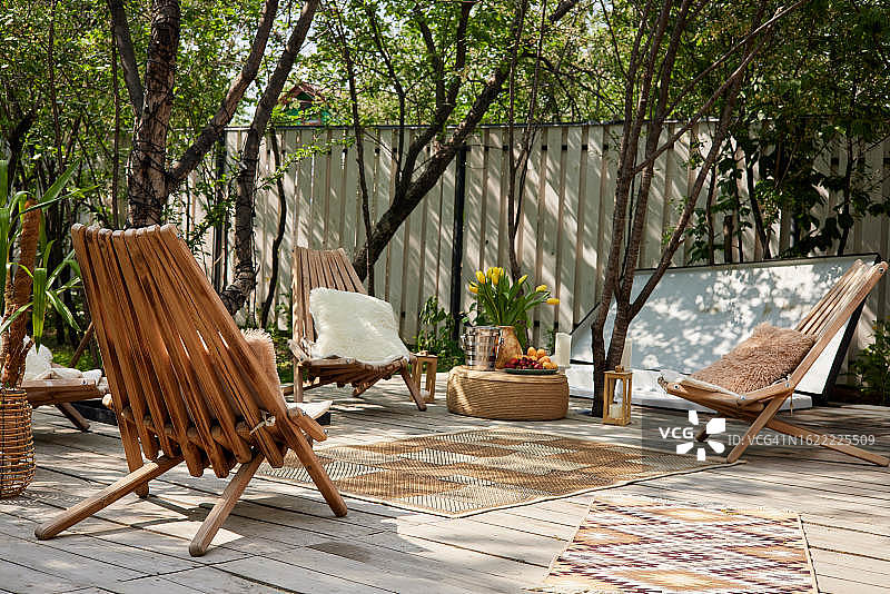 阳光下绿树旁的木制扶手椅与地毯图片素材