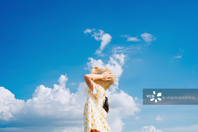可爱亚洲小女孩戴着草帽站在户外，沐浴在阳光下（仰视角度）图片素材