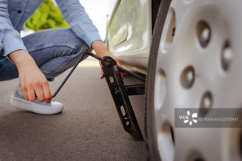在路上用千斤顶快速更换轮胎的年轻女人图片素材